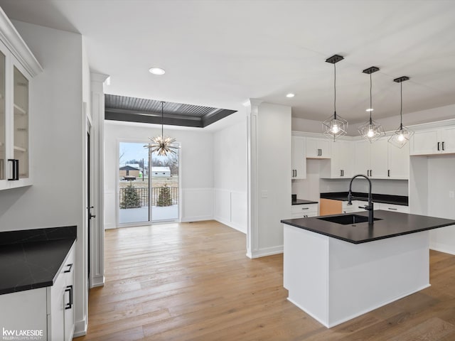 kitchen featuring sink, a center island with sink, white cabinets, a chandelier, and hanging light fixtures