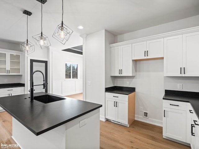 kitchen featuring white cabinets, a center island with sink, hanging light fixtures, and sink