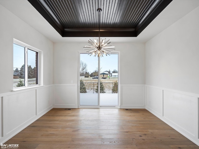 unfurnished dining area featuring a raised ceiling, a chandelier, and wood-type flooring