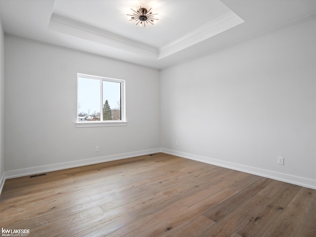 spare room featuring light hardwood / wood-style floors and a raised ceiling