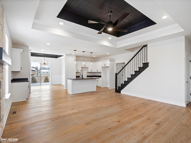 unfurnished living room with ceiling fan, light hardwood / wood-style floors, sink, and a tray ceiling