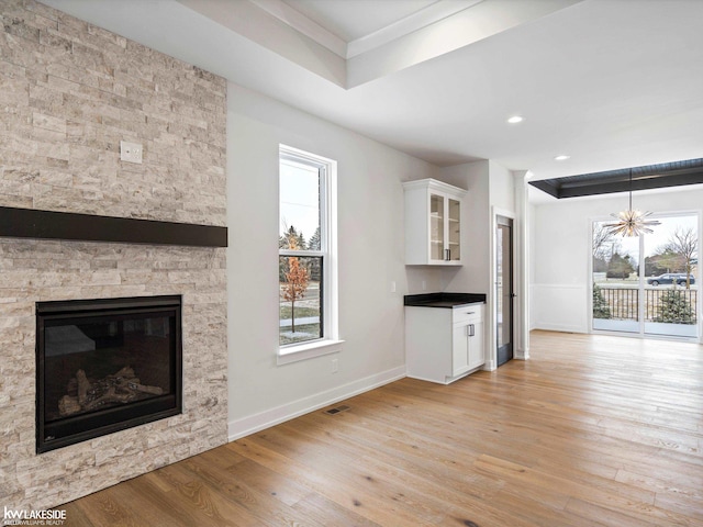 unfurnished living room with an inviting chandelier, light wood-type flooring, a fireplace, and a tray ceiling