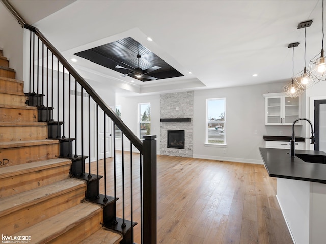 interior space with a raised ceiling, sink, ceiling fan, a fireplace, and wood-type flooring