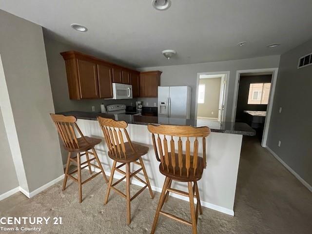 kitchen featuring electric range oven, stainless steel fridge with ice dispenser, kitchen peninsula, and a breakfast bar