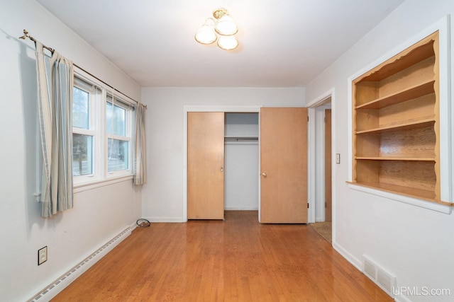 unfurnished bedroom with light wood-type flooring, a closet, and baseboard heating