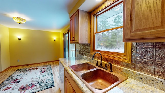 kitchen with sink, dishwasher, light stone counters, light hardwood / wood-style flooring, and decorative backsplash