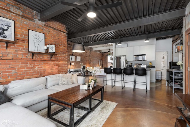 living room featuring ceiling fan, beamed ceiling, and brick wall