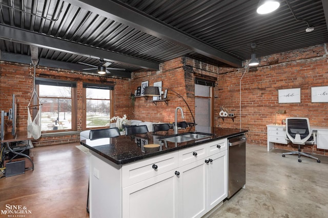 kitchen with sink, beamed ceiling, brick wall, dark stone counters, and white cabinets