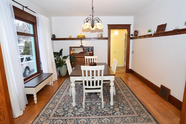 dining space with hardwood / wood-style floors, a textured ceiling, and an inviting chandelier