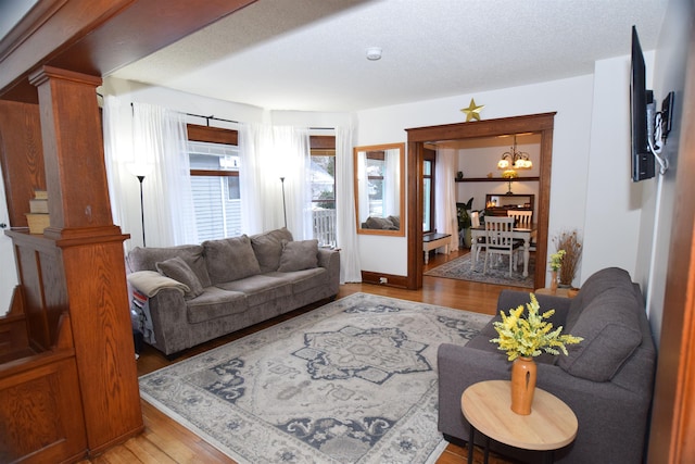 living room featuring light hardwood / wood-style floors, ornate columns, a textured ceiling, and an inviting chandelier