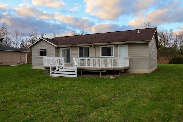 back house at dusk featuring a lawn and a deck