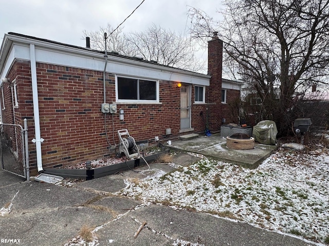 snow covered rear of property with a patio and a fire pit