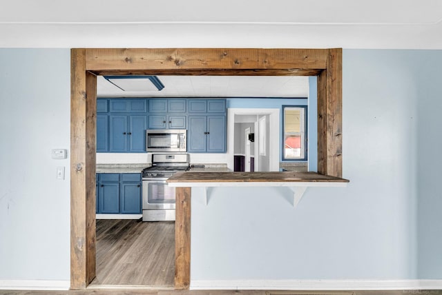 kitchen featuring kitchen peninsula, appliances with stainless steel finishes, dark hardwood / wood-style flooring, blue cabinetry, and a breakfast bar area