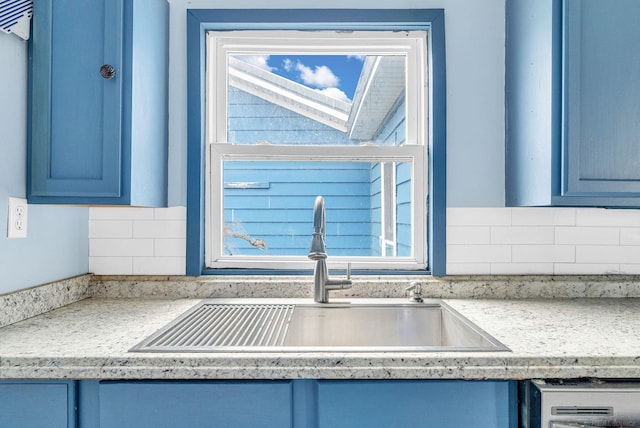 interior details featuring blue cabinetry, decorative backsplash, sink, and light stone counters