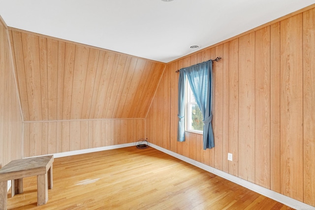 unfurnished room featuring wood-type flooring, wooden walls, and lofted ceiling