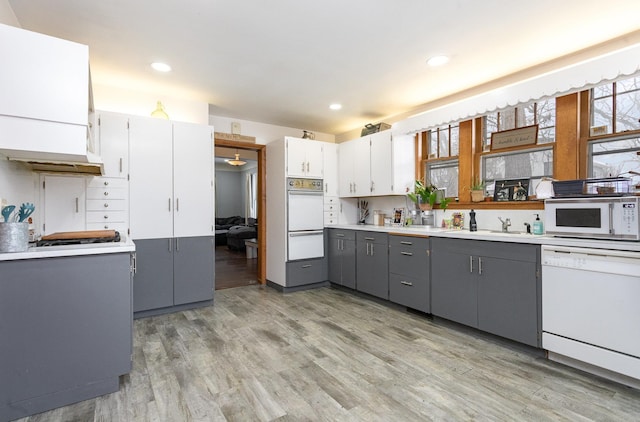 kitchen with gray cabinetry, sink, light hardwood / wood-style floors, white appliances, and white cabinets