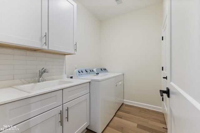 clothes washing area with washing machine and clothes dryer, light hardwood / wood-style flooring, cabinets, and sink