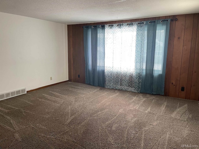 spare room with carpet flooring, a textured ceiling, and wooden walls