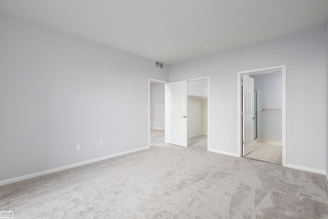 unfurnished bedroom with ensuite bath, a spacious closet, a closet, and light colored carpet