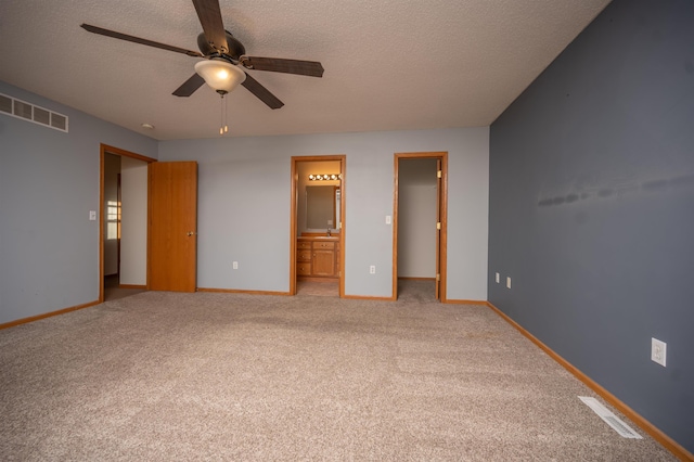 unfurnished bedroom with light carpet, a walk in closet, ensuite bath, a textured ceiling, and ceiling fan