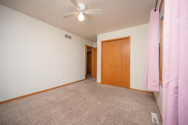 unfurnished bedroom with a textured ceiling, light colored carpet, a closet, and ceiling fan