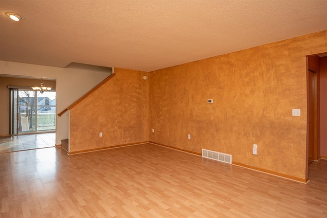 unfurnished living room featuring hardwood / wood-style floors, a textured ceiling, and an inviting chandelier