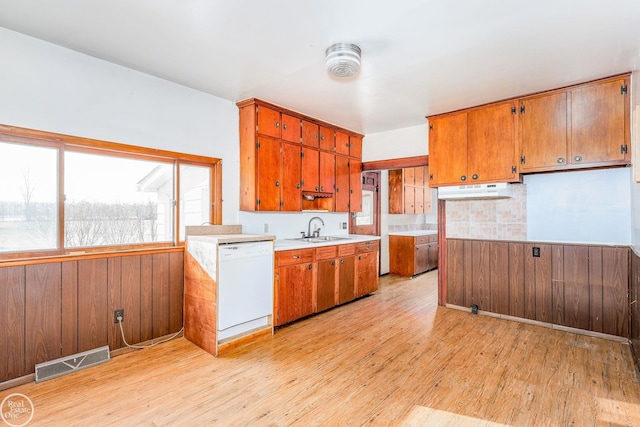 kitchen with wooden walls, dishwasher, light hardwood / wood-style floors, and sink