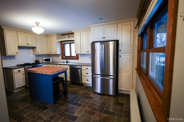 kitchen with wooden counters, decorative backsplash, stainless steel appliances, sink, and a kitchen island