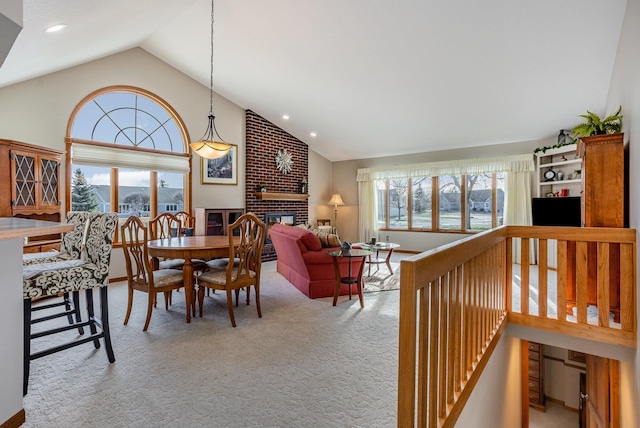 dining space with light carpet, vaulted ceiling, a brick fireplace, and a wealth of natural light