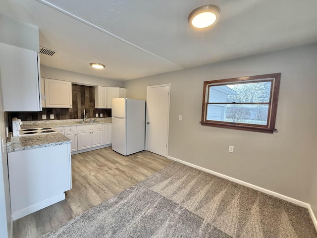 kitchen with white cabinetry, sink, light stone countertops, stove, and white fridge