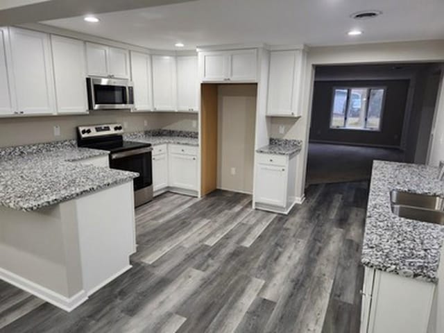 kitchen featuring white cabinets, dark hardwood / wood-style floors, light stone counters, and appliances with stainless steel finishes