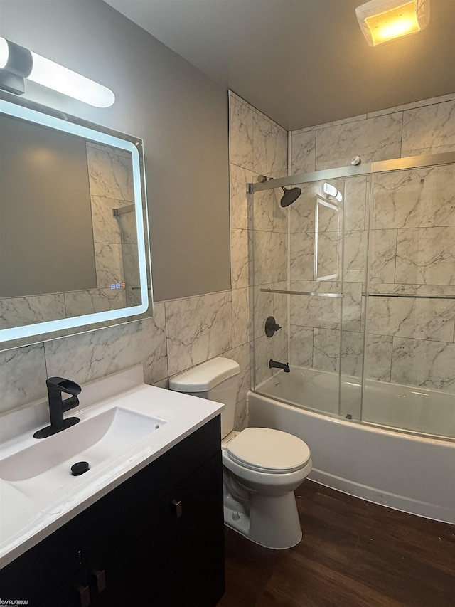 full bathroom featuring vanity, hardwood / wood-style flooring, tile walls, enclosed tub / shower combo, and toilet