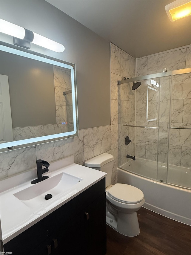 full bathroom featuring combined bath / shower with glass door, vanity, wood-type flooring, tile walls, and toilet