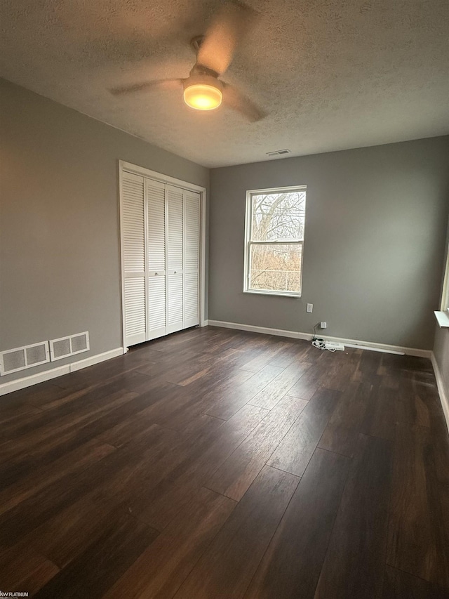 unfurnished bedroom featuring ceiling fan, dark wood-type flooring, a textured ceiling, and a closet