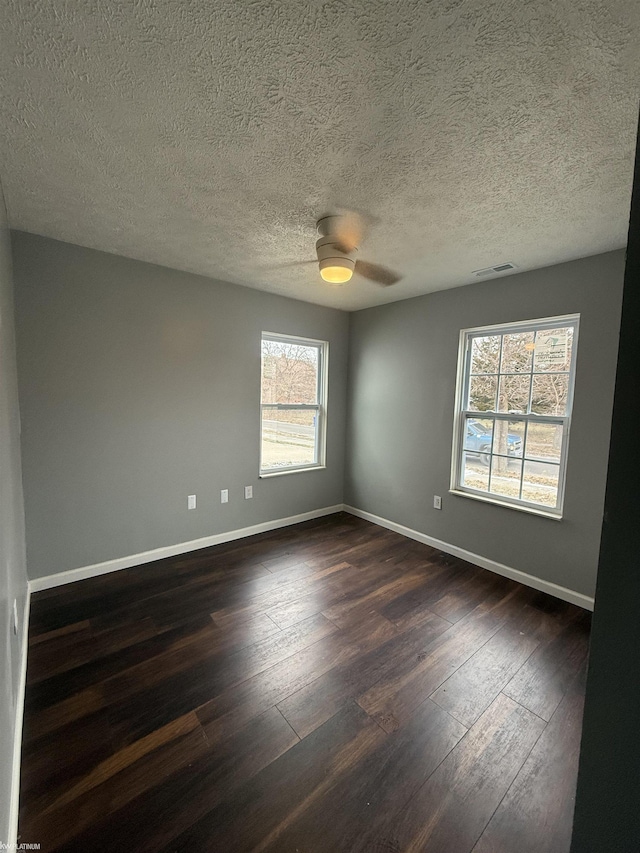 spare room featuring dark hardwood / wood-style floors, ceiling fan, a textured ceiling, and a wealth of natural light