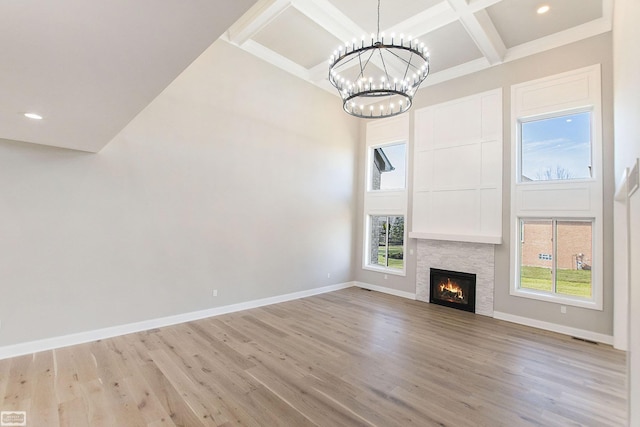 unfurnished living room featuring a towering ceiling, light hardwood / wood-style flooring, a stone fireplace, and coffered ceiling