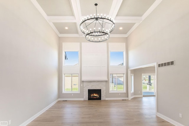 unfurnished living room featuring a fireplace, a towering ceiling, a chandelier, and light hardwood / wood-style floors