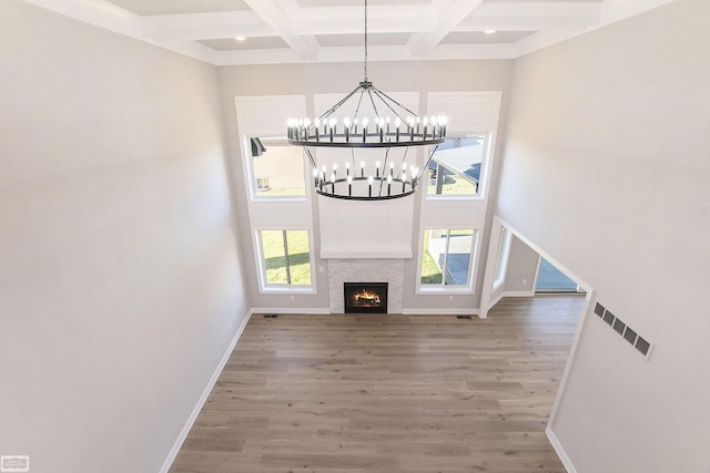 unfurnished living room featuring coffered ceiling, hardwood / wood-style flooring, beamed ceiling, a chandelier, and a stone fireplace