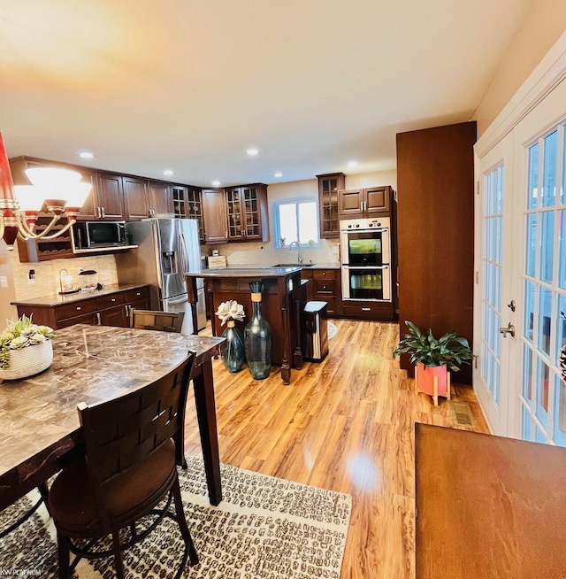 interior space featuring sink, french doors, backsplash, light hardwood / wood-style floors, and appliances with stainless steel finishes