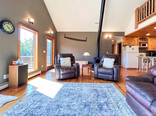 living room featuring light wood-type flooring, a wood stove, baseboard heating, and high vaulted ceiling