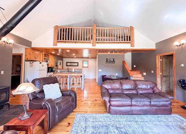 living room with a towering ceiling, sink, light hardwood / wood-style flooring, wooden ceiling, and a wood stove