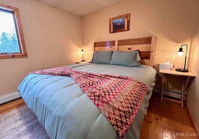 bedroom with hardwood / wood-style floors and a baseboard heating unit