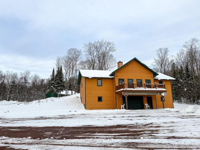 snow covered house featuring a garage and a balcony