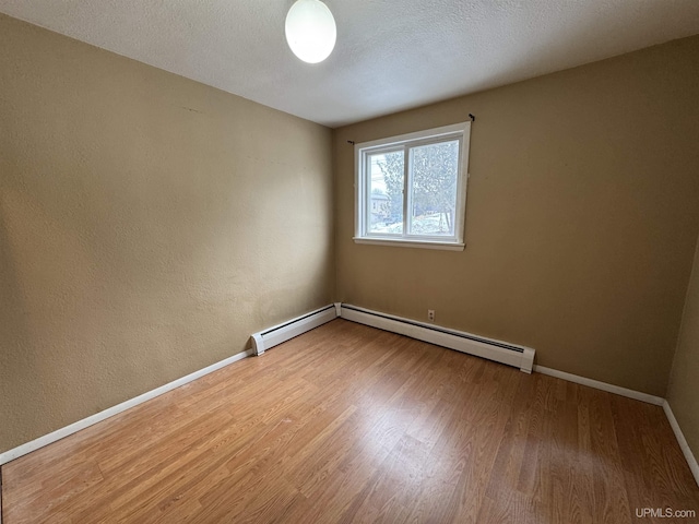 spare room featuring a textured ceiling, hardwood / wood-style flooring, and a baseboard heating unit