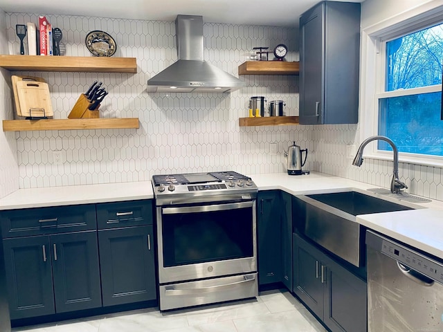 kitchen with sink, stainless steel appliances, wall chimney range hood, tasteful backsplash, and blue cabinets