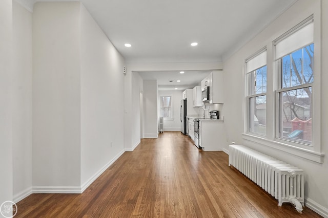 hall with plenty of natural light, light wood-type flooring, crown molding, and radiator