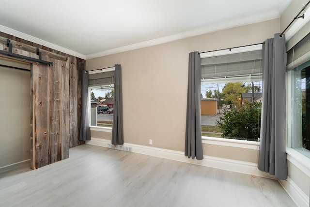 empty room with a barn door, light hardwood / wood-style flooring, a wealth of natural light, and ornamental molding