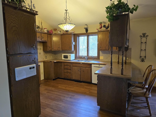 kitchen featuring pendant lighting, lofted ceiling, white appliances, dark wood-type flooring, and sink