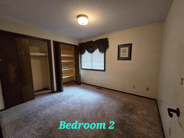 unfurnished bedroom with a textured ceiling, two closets, and carpet floors