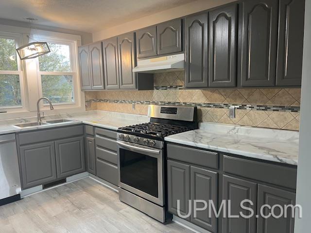 kitchen with light stone countertops, appliances with stainless steel finishes, gray cabinetry, sink, and light hardwood / wood-style floors